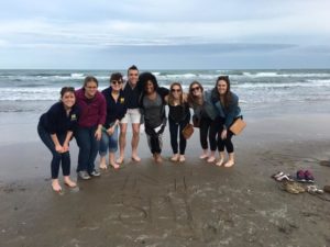 After writing “SPH” and a block “M” in the sand, School of Public Health spring break students take a photo at South Padre Island upon their arrival for a community health assessment project in Hidalgo County, Texas. They are, from left, Liz Timoszyk, Elana Elkin, Peggy Korpela, Christopher Bush, Megan Edmonds, Chelsea Abshire, Grace Christensen and Julia Porth. Photo Courtesy of the School of Public Health 