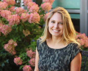 Young female student Riley Nelson standing in front of flowered bush