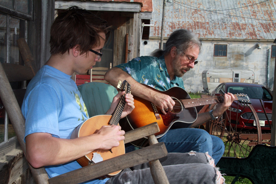 A student and a professor play instruments (guitar and mandolin) on a country porch