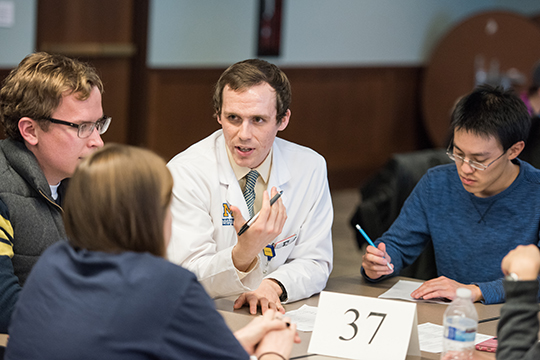 Three students sit around a table while a doctor speaks to them