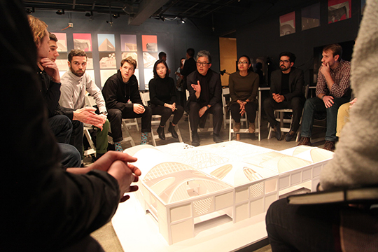 Eleven people sit around a styrofoam model of a building