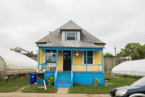 A small, bright house. The walls are painted vibrant yellow and the stairs, foundation, and thin columns on the porch are painted a bright blue.