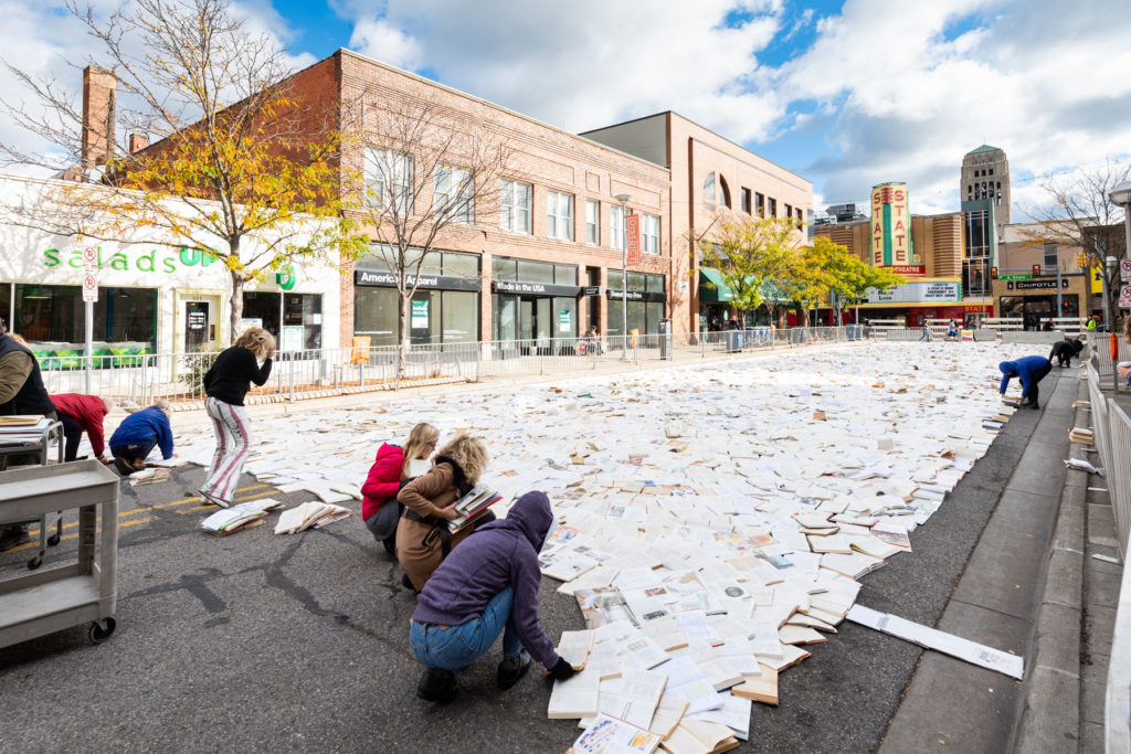 Several people work to distribute books evenly across Liberty Street next to Salads up, where they have progressed from their starting point at State theater.