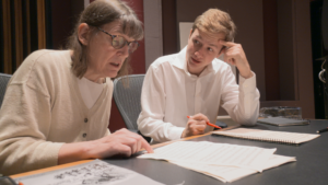 Student and teacher converse over music sheets.