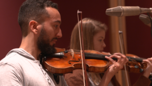 A male and female student play their violins with great focus.