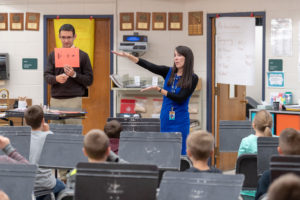 Kellie and Joe stand in front of the class holding a piece of paper with a half note, quarter rest, and quarter note, and Kellie motions with her hands.