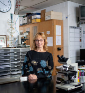 Racquel Huddleston stands in her lab, looking slightly to the right of the camera with a slight smile.