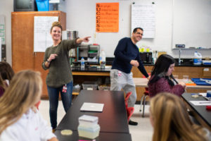 Nye points to a student in the classroom, while Simmons stands smiling in the background.