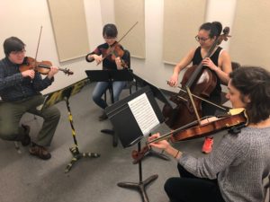 Four students play string instruments. 