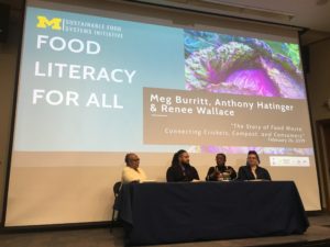 Panel sits in front of screen that reads "Food Literacy for All."