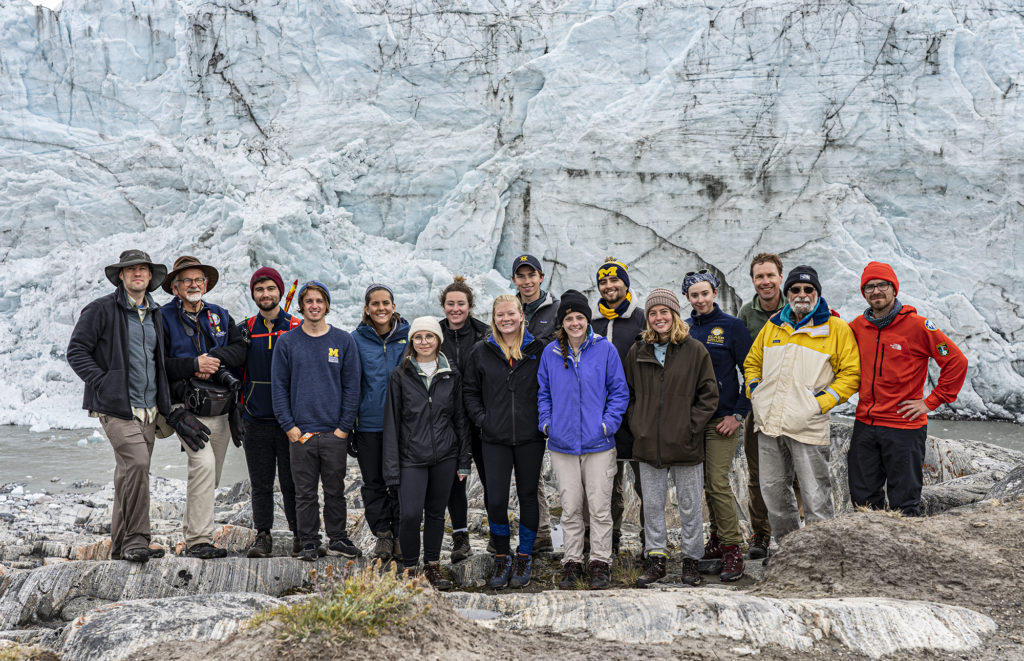 A group of people pose in front of a glacier. 