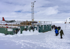 A group of people walk through snow to a building with equipment. 