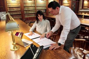 Woman sits at desk with flute, director's batons and music in front of her and show it to a man.