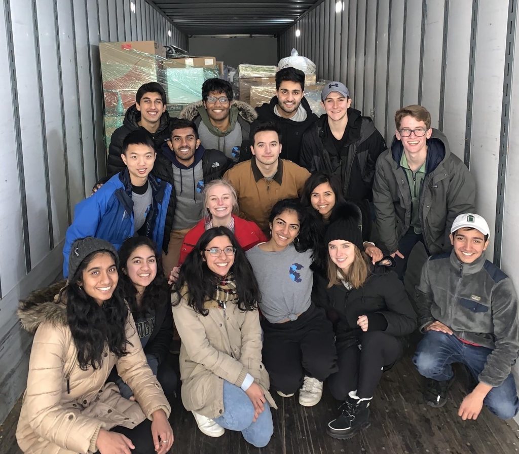 A group of students pose together inside a box truck with supplies in the background.