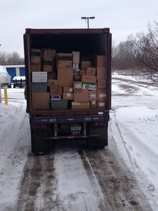 Open box truck filled with cardboard boxes in a snowy parking lot.