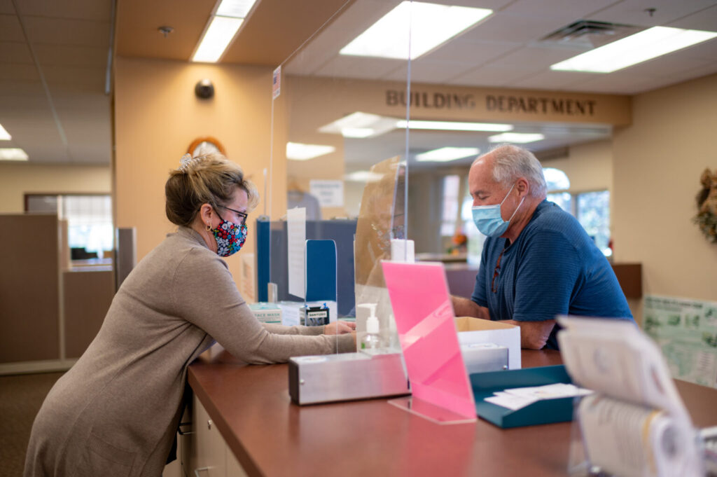 A person is at a counter speaking to someone on the other side with a plastic divider in between. 