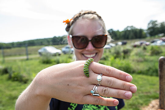 Young girl wearing sunglasses holds a caterpillar up to the camera