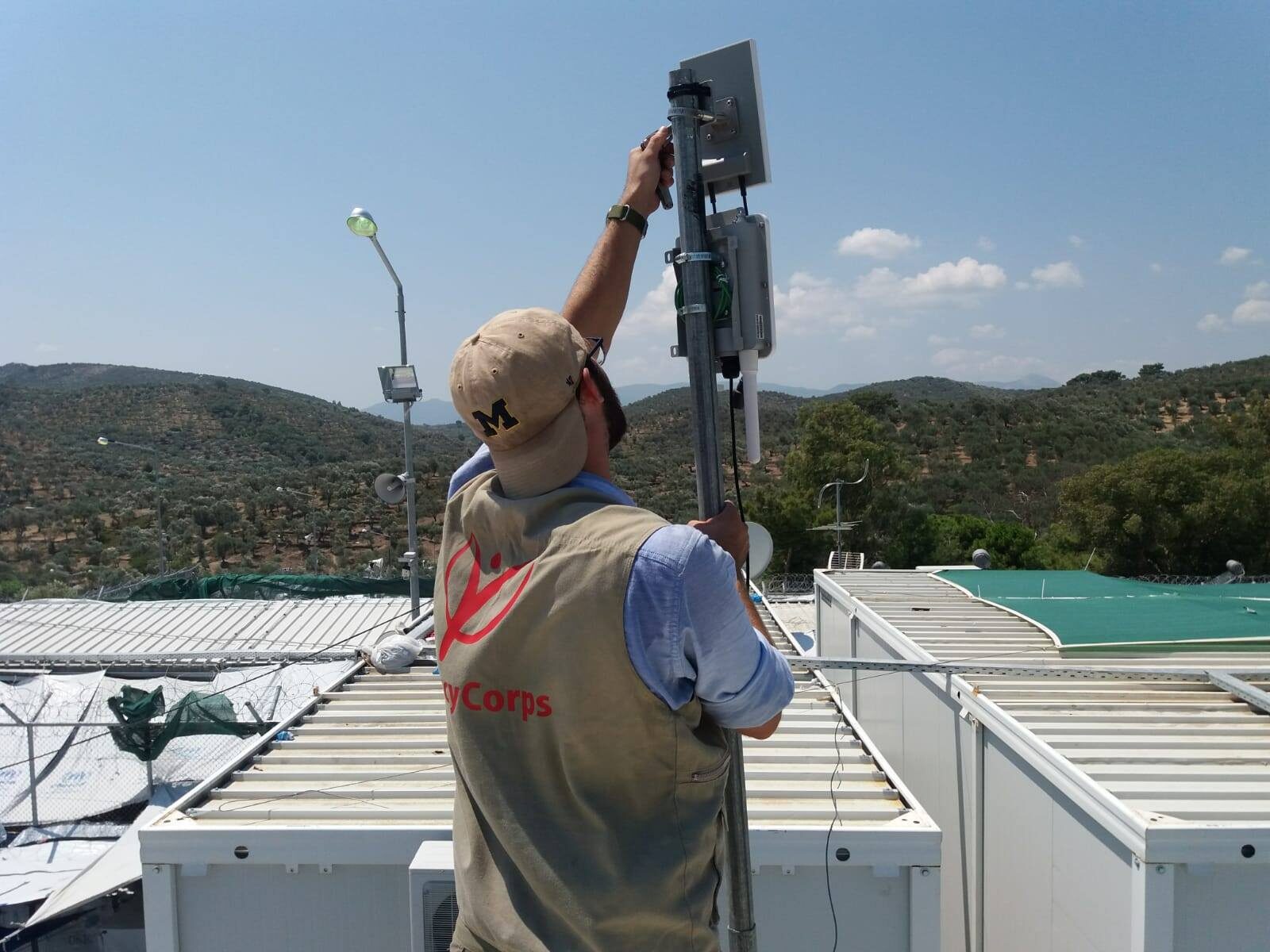 Traylor's back faces the camera as he bolts down the access point. Greece's mountains and blue water are visible in the background.