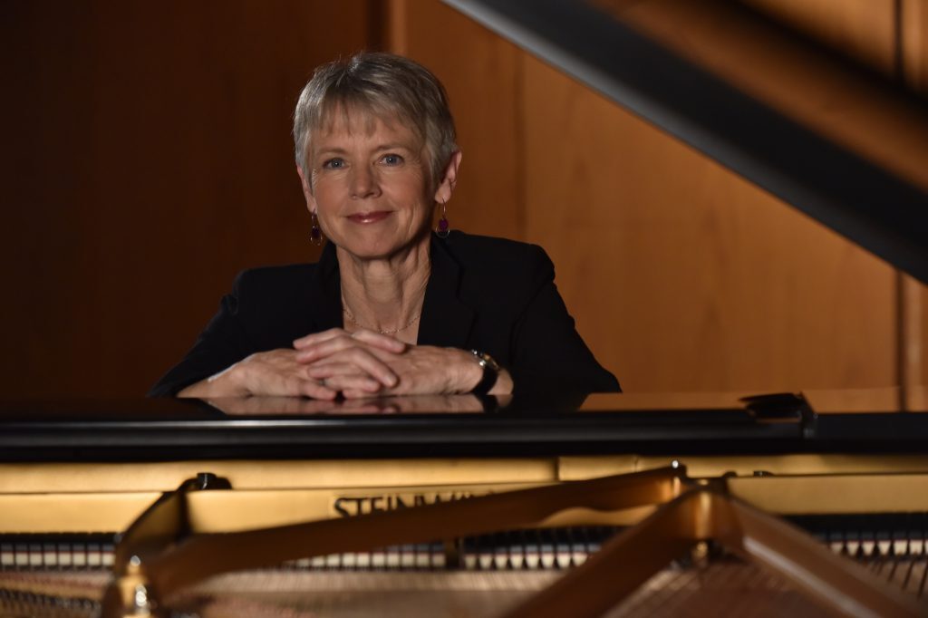 Ellen poses sitting at a piano.