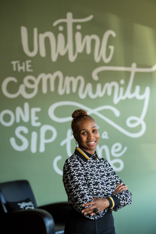 Jevona stands in front of a sign reading: uniting community one sip at a time.