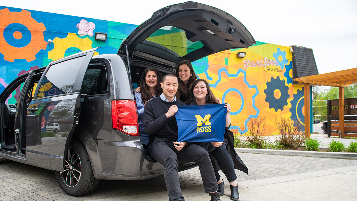 Students pose in the trunk of a van holding a flag that reads "M Ross."